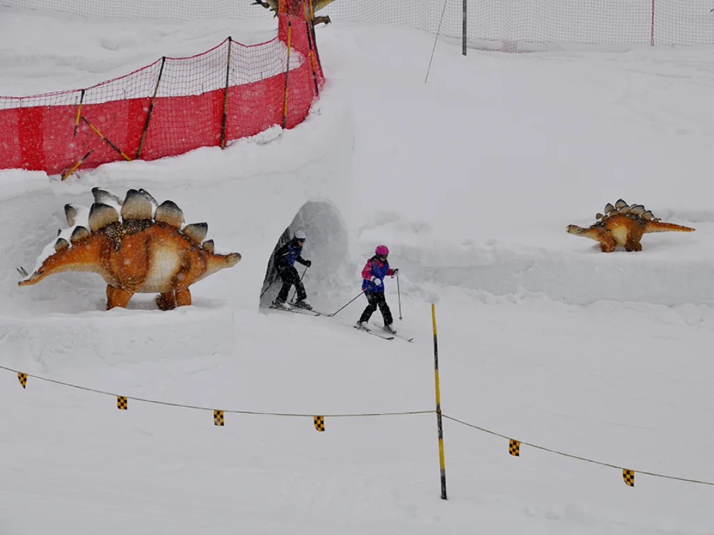 Kinderland mit Dinosaurierfiguren am Pistenrand.